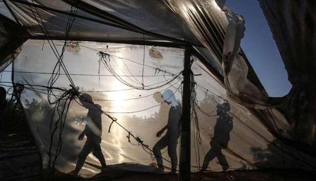 Palestinian men walk behind a greenhouse damaged by an Israeli airstrike launched in response to rocket fire, in Khan Yunis in the southern Gaza Strip