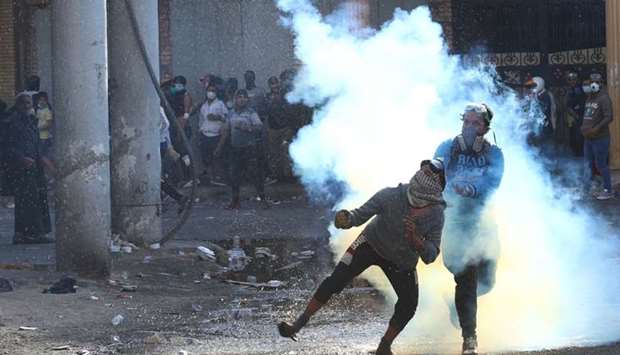 An Iraqi demonstrator throws away a tear gas canister during the ongoing anti-government protests in Baghdad, Iraq