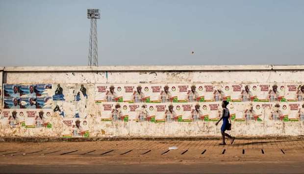 A woman walks past election campaign posters on the eve of the presidential elections in Guinea-Bissau