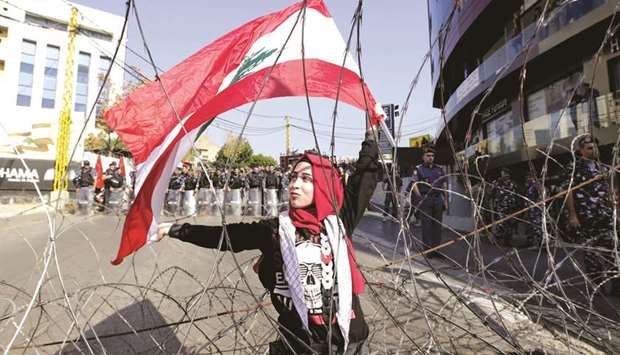 A Lebanese demonstrator waves the national flag while security forces stand by during a protest in Awkar, northeast of the Beirut, yesterday.