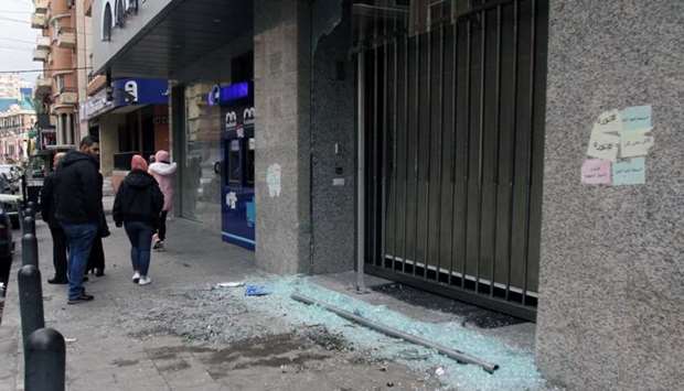 Men walk near broken glass from a damaged Bankmed branch in Tripoli, Lebanon