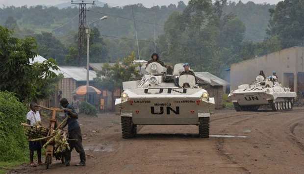 Congolese men push their makeshift bicycle past UN peacekeepers