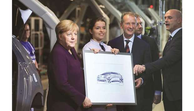 Germanyu2019s Chancellor Angela Merkel (left) poses for photographs while holding a sketch of a Volkswagen ID.3 electric automobile with Herbert Diess, CEO of VW (second right), in Zwickau, Germany, yesterday. Merkelu2019s visit to the factory in the eastern state of Saxony marks the production start for the VW brandu2019s first mass-market vehicle based on a technology developed solely for battery-powered cars.