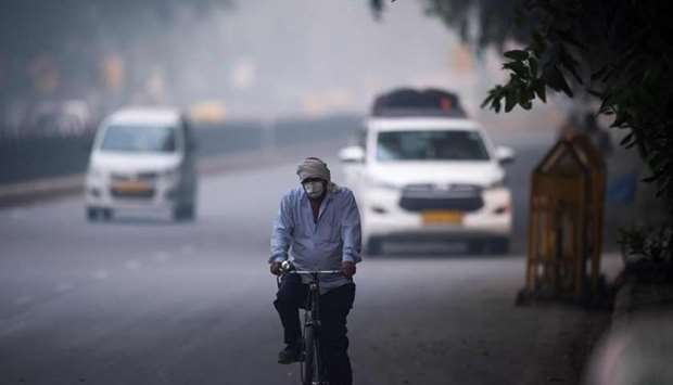 A man wearing protective face mask rides a bicycle along a street in smoggy conditions in New Delhi