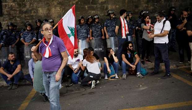 A protester carries a flag as he stands in front of police officers outside of the Ministry of Foreign Affairs and Emigrants during a protest in Beirut