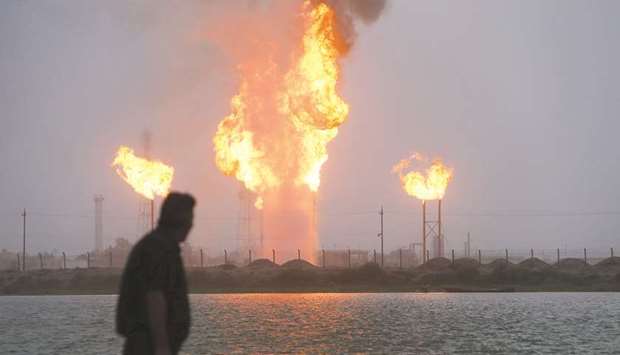 A man looks at flames rising from oil refinery pipes in Basra, Iraq. Opec+ nations that flouted their output quotas in the initial months of the agreement, such as Iraq and Nigeria, have been tasked with u201ccompensation cuts.u201d