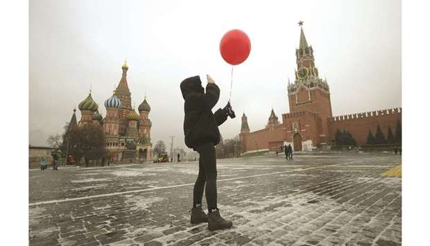 A woman wearing a protective face mask uses her smartphone while holding an air balloon on an almost-empty Red Square in Moscow yesterday.