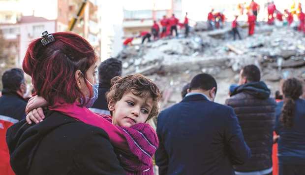 A woman holds her child as volunteers and rescue personnel search yesterday for survivors in a collapsed building in Izmir.