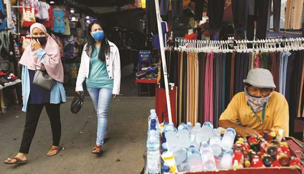 Women wearing protective masks walk as a drinks vendor sits waiting for the customers at Tanah Abang textile market, following the outbreak of coronavirus disease in Jakarta.