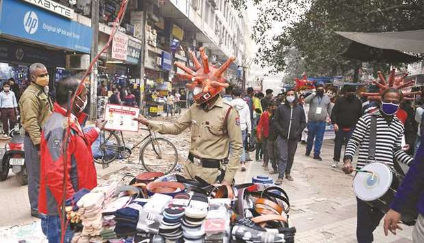 A civil defence volunteer wearing a Covid-19 coronavirus-themed helmet distributes a placard to a vendor during an awareness campaign at a market in New Delhi yesterday.