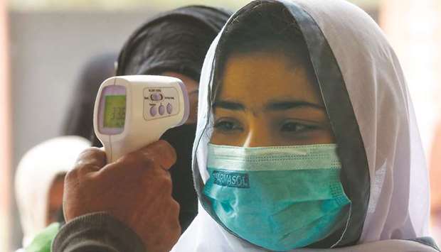A school official checks the body temperature of a student wearing face mask as she enters a school amid the Covid-19 coronavirus pandemic in Karachi yesterday. (AFP)