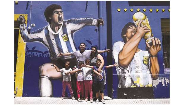 A family poses with murals depicting late Argentinian football legend Diego Maradona, outside Boca Juniorsu2019 stadium in Buenos Aires yesterday. Maradona died of a heart attack on Wednesday at the age of 60. (AFP)