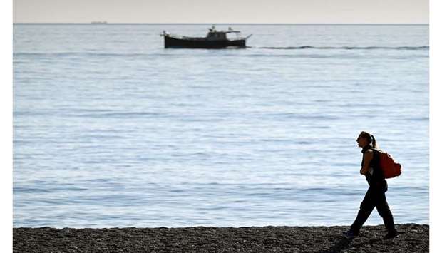 A woman, wearing a protective face mask, walks along the sea in Varazze.