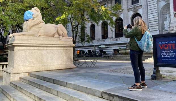 A woman takes a photo of the he u201cPatience and Fortitudeu201d marble lion, wearing a mask, at the New York public library building  in New York.