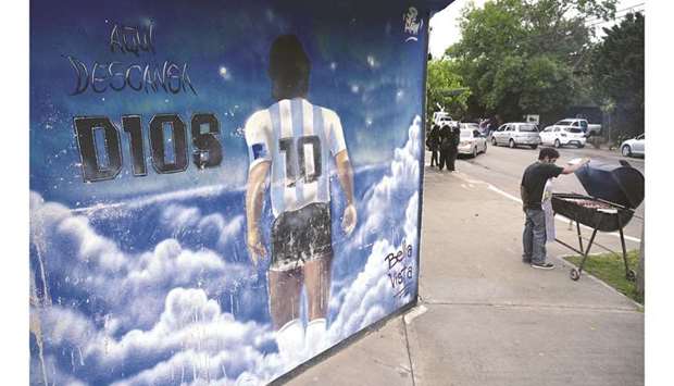 A man prepares barbecue next to a mural that reads u2018Here rests D10Su2019 outside the private cemetery where Argentine late footballer Diego Maradona is buried, on the first anniversary of his death, in Bella Vista, Buenos Aires province, Argentina, yesterday. (AFP)