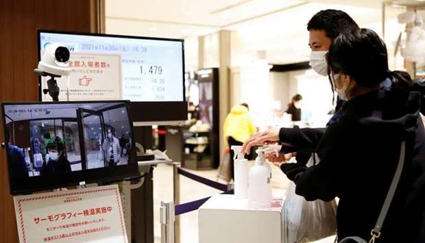 People disinfect their hands while a thermal camera reads their temperature, at the entrance of a department store, on the first day of Japan's closed borders to prevent the spread of the Omicron variant of coronavirus, in Tokyo. REUTERS