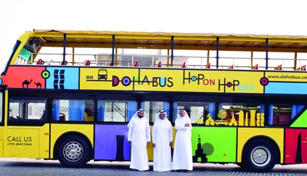Amlak and Doha Bus officials in front of a sightseeing tour bus