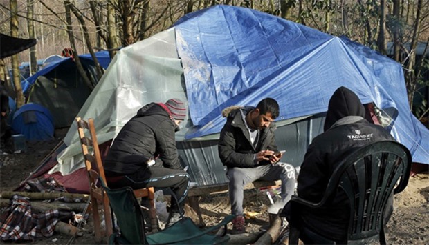 A migrant checks his mobile phone next to shelters