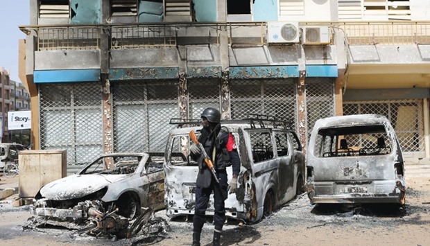 A soldier stands guard in front of burned cars across the street from Splendid Hotel in Ouagadougou.