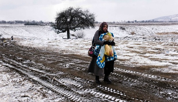 A migrant woman carries her baby as she walks through a snowy field, after crossing the Macedonian border into Serbia near the village of Miratovac on January 18, 2016.  More than one million migrants reached Europe in 2015, most of them refugees fleeing war and violence in Afghanistan, Iraq and Syria, according to the United Nations refugee agency.  AFP
