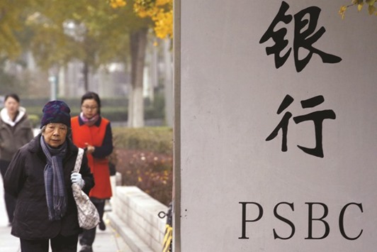 People walk past a signboard outside a branch of Postal Savings Bank of China in downtown Beijing. The firm has invited investment banks to pitch for a Hong Kong IPO worth up to $15bn, sources said yesterday.