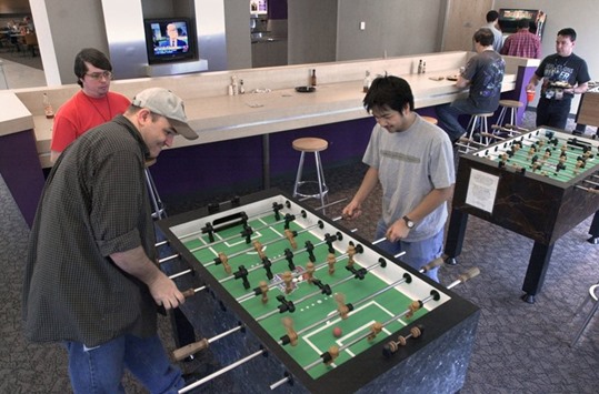 Employees playing a game of foosball in an office. We are living in the Decade of Perks. Companies are falling over one another offering workers such goodies as squash courts, hoverboards, lap pools, nap zones, pet care and more.