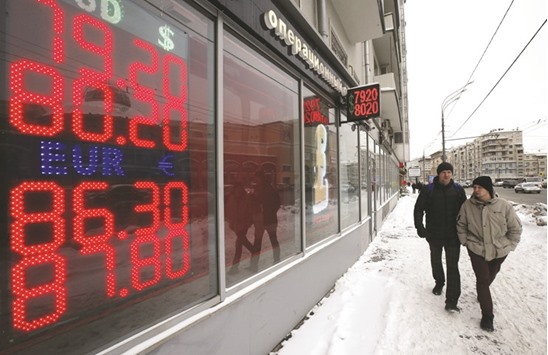 Men walk past a board showing currency exchange rates of the US dollar and euro against the rouble in Moscow. The Russian currency set a low of 80.92 against the greenback yesterday.