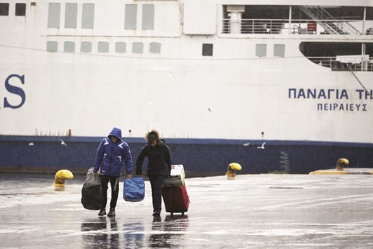 Passengers carry their luggage under heavy rain as passenger ships are moored during a 48-hour strike by Greek ship workers against planned pension reforms at the port of Piraeus, near Athens.