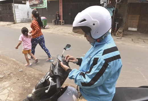 A female motorcycle taxi driver checking for an order on her smartphone in Jakarta.