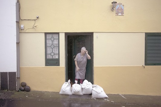SURVIVAL INSTINCT: A woman stands as sandbags are placed outside houses to protect against heavy rains and winds during the passage of Hurricane Alex in Ponta Delgada, Azores, Portugal.