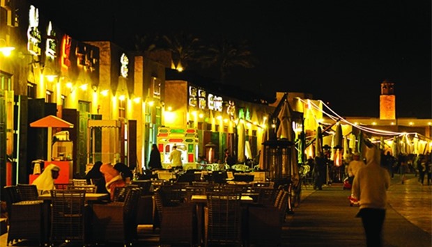 A man walks past customers of Souq Al Wakrah, which is gaining popularity for its scenic Corniche an