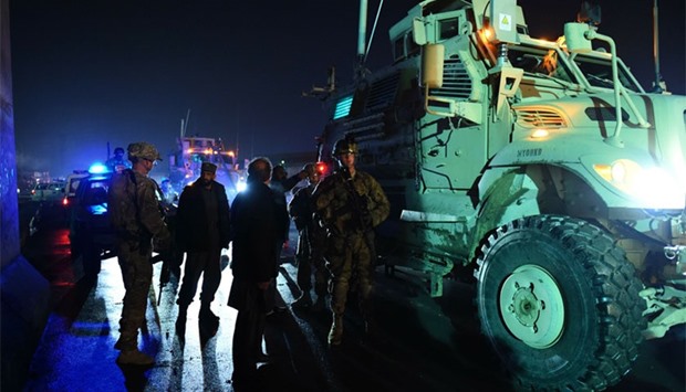 US soldiers and Afghan security forces stand next a military vehicle as they arrive at the site of a suicide car bomb attack that targeted a compound for foreign contractors near the international airport in Kabul