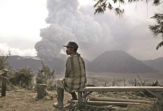 A local resident rests on a bench as Mount Bromo volcano erupts in the background in Ngadisari, Probolinggo, East Java, Indonesia, yesterday.