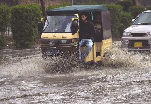 A Pakistani passenger sits in an autorickshaw while crossing a flooded street after heavy rain in Karachi yesterday.