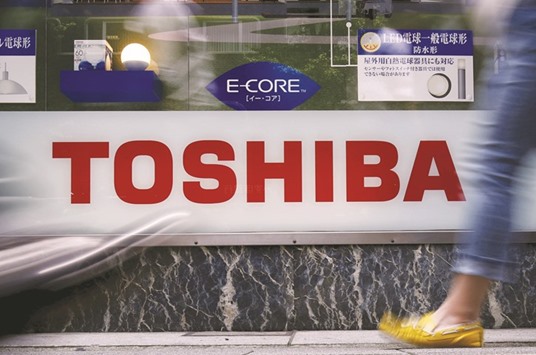 A pedestrian walks past a logo of Toshiba outside an electronics retailer in Tokyo. The company wants to sell a minority stake in its core semiconductor business and is considering potential buyers including US partner Western Digital Corp, a source said.