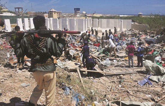 Civilians and soldiers stand amongst scattered objects and belongings at the scene of a car bomb attack near Mogadishuu2019s Peace Hotel.