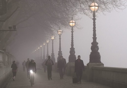 People walk along The Embankment during a foggy morning in London.