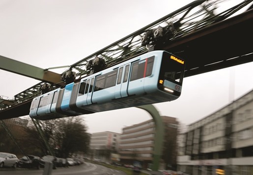 A new train car rides the Wuppertal suspended monorail track across a road.