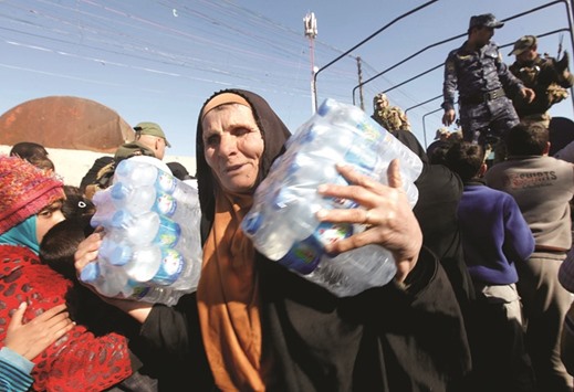 An elderly woman carries bottles of water she received from Iraqi security forces in Antesaar neighbourhood of Mosul, Iraq yesterday.