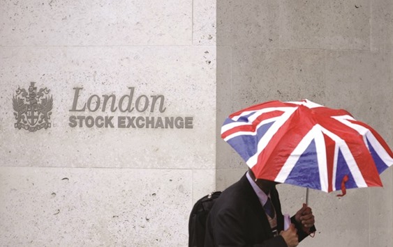 A worker shelters from the rain under an umbrella as he passes the London Stock  Exchange. The FTSE 100 gained 0.2% to 7,164.43 points yesterday.