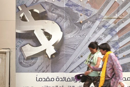 Pedestrians walk past an advertisement displaying a large dollar sign and US dollar banknotes outside a bank in Cairo. Egypt floated its currency in November, slashing its value by half, in a bid to attract foreign investment and stimulate an economy that has suffered from shrinking business activity for 15 months.