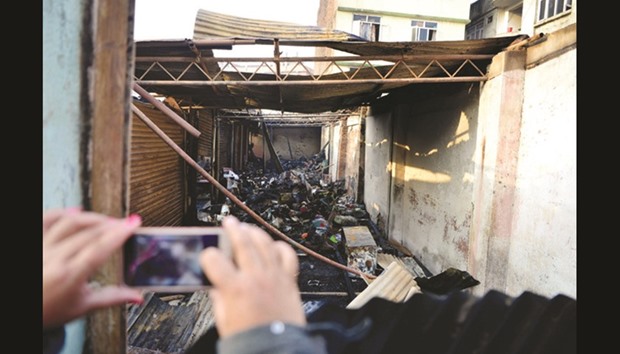 A Nepalese bystander takes photographs with her mobile phone of a burnt out shop following a fire, in Kuleshwor market in Kathmandu yesterday. No casualties were reported in the fire.