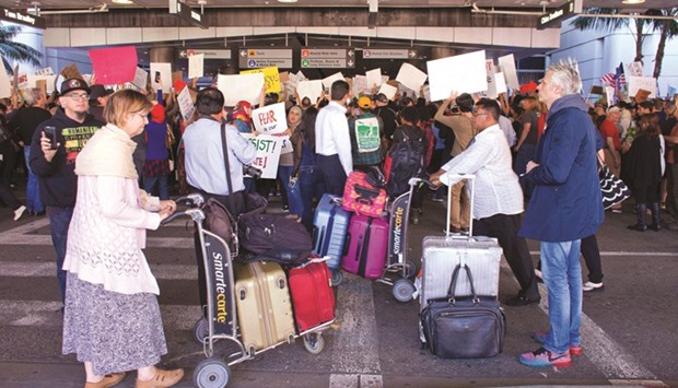 Travellers stand outside Los Angeles International airportu2019s Tom Bradley terminal as protesters demonstrate against President Trumpu2019s executive order banning citizens from seven Muslim countries.