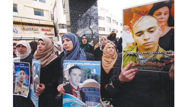 Rajaa (centre), holds a poster of her son Abdul Fatah al-Sharif as Palestinians gather in the street in the West Bank town of Hebron yesterday, during the trial of Israeli soldier Elor Azaria (portrait-right) who killed Sharif, as he lay on the ground posing no apparent threat.