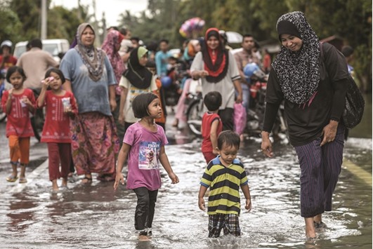 Local residents wade through a flooded street in Jal Besar, Malaysiau2019s northeastern town of Tumpat. Floods continued to inundate two northeast Malaysian states yesterday, as thousands of people remained in relief centres while others expressed fears of looting and sought aid.