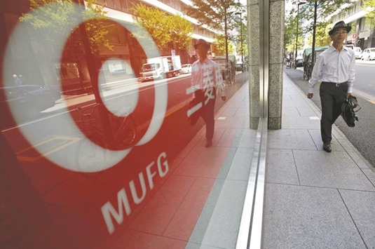 A pedestrian walks next to a logo of the Mitsubishi UFJ Financial Group outside a branch of its bank in Tokyo. The MUFG says itu2019s ready to compete with the biggest banks on Wall Street in fixed income after adding teams for trading mortgage-backed securities and underwriting non-investment grade debt in the US in 2016.