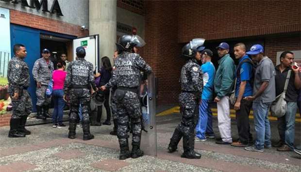 Police officers control the crowd as people line up to buy sugar, outside a supermarket in Caracas.