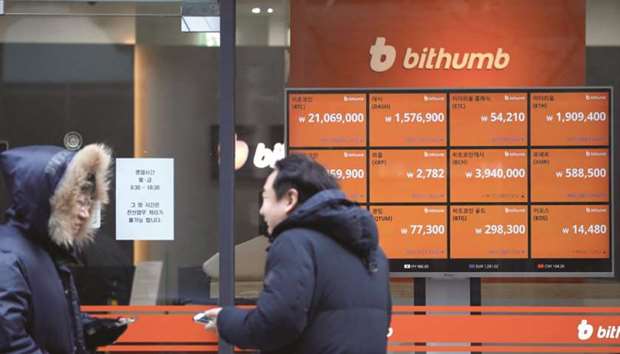 Men talk in front of an electronic board showing exchange rates of various cryptocurrencies at Bithumb exchange in Seoul. The local price of bitcoin plunged as much as 21% in midday trade to 18.3mn won ($17,064.53) yesterday.