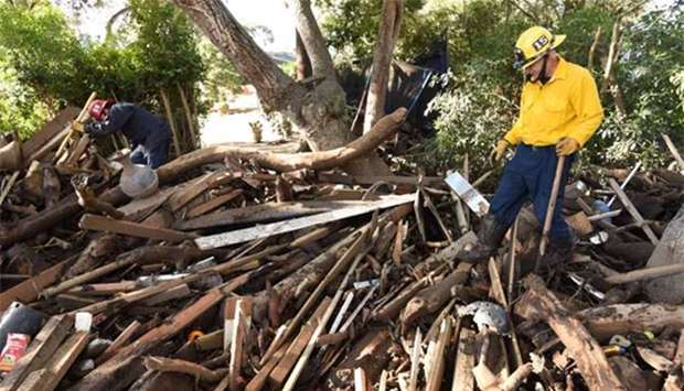 Santa Barbara County Fire staff search through a debris pile behind a home destroyed by mudflow and debris in Montecito, California.