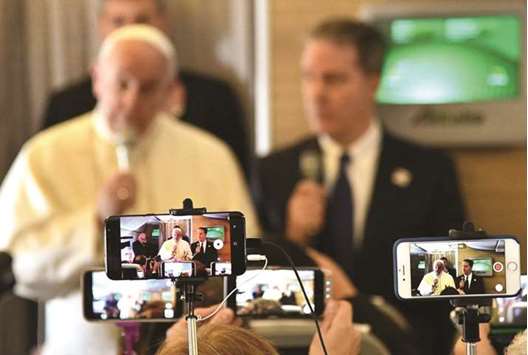 Journalists use their phones to record a video as Pope Francis delivers a press conference aboard the papal plane.